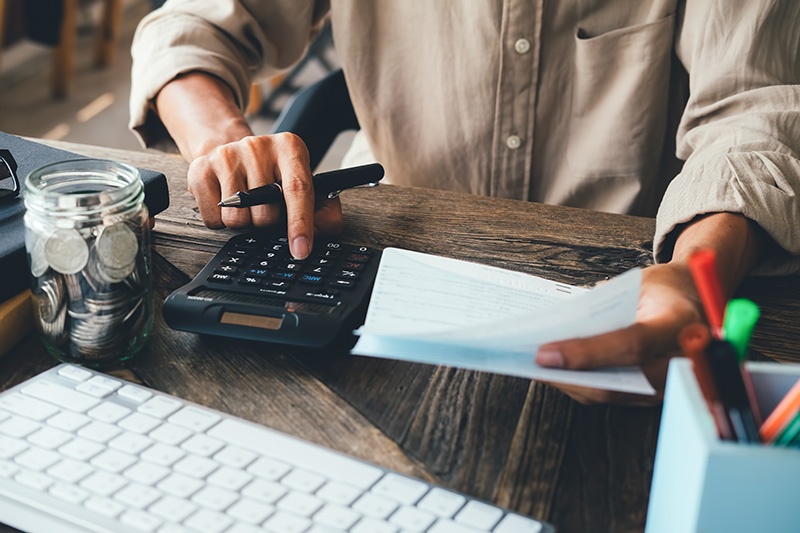 Person calculating expenses with a calculator and bills on a desk.