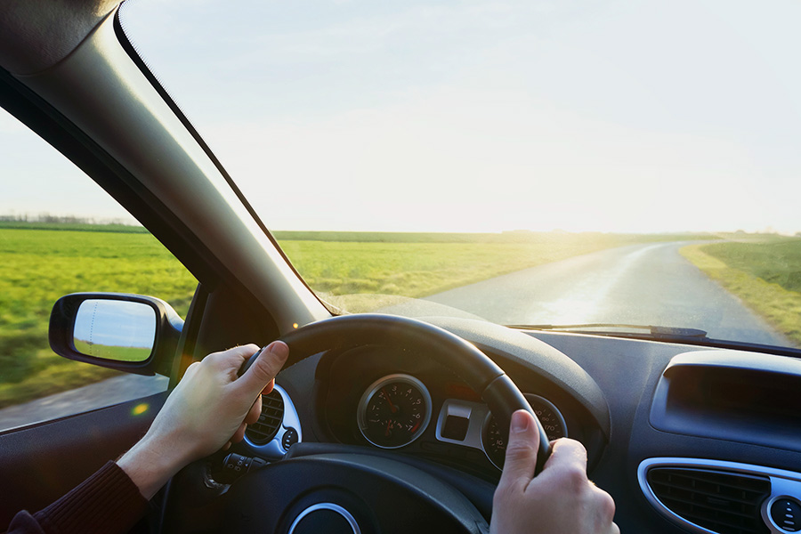 Driver’s view of hands on a steering wheel on an open road.