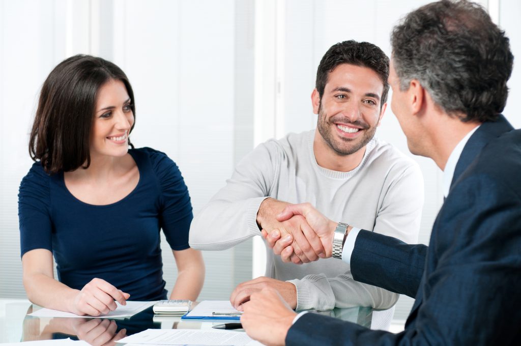 A man and a woman smiling while shaking hands in a meeting.